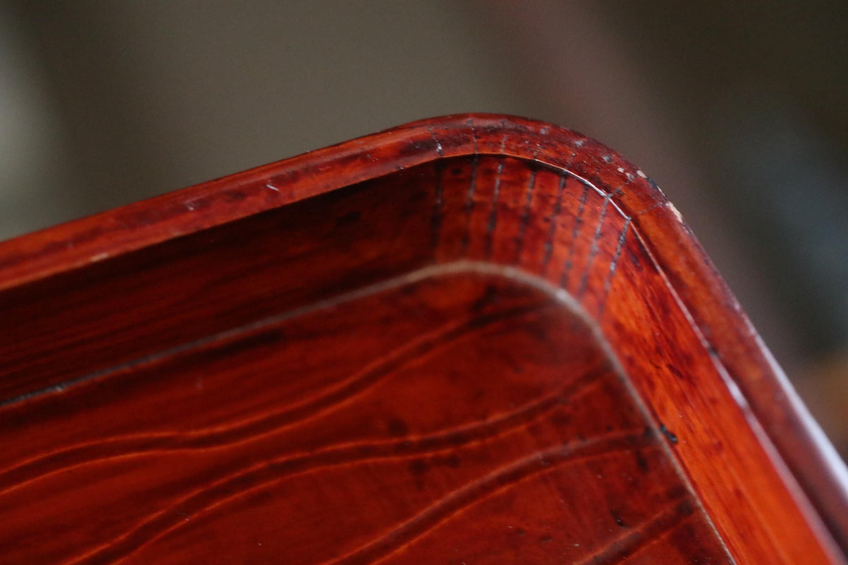 A close-up view of a wooden surface with a rich, reddish-brown hue, featuring a textured, wavy pattern.