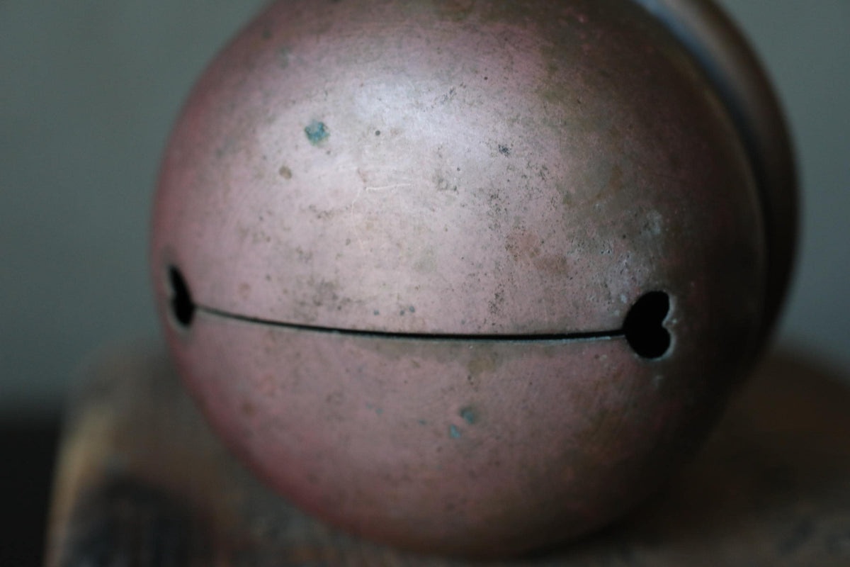 A close-up image of a round, metallic bell with a heart-shaped hole in the center.