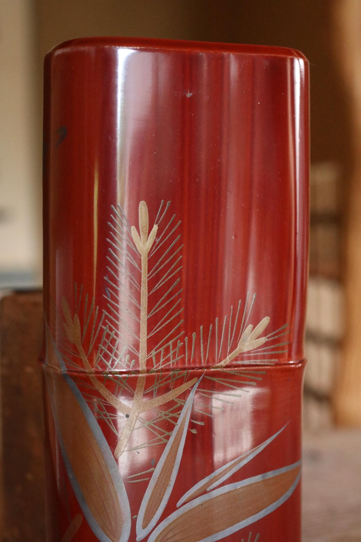 A close-up image of a red vase with a decorative design featuring a pine tree and leaves.