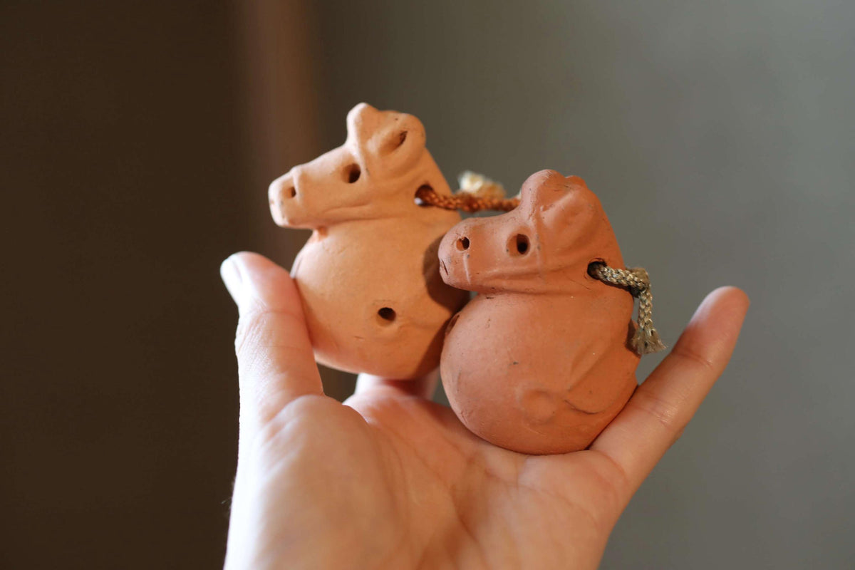 A hand holding two small clay figurines of pigs.