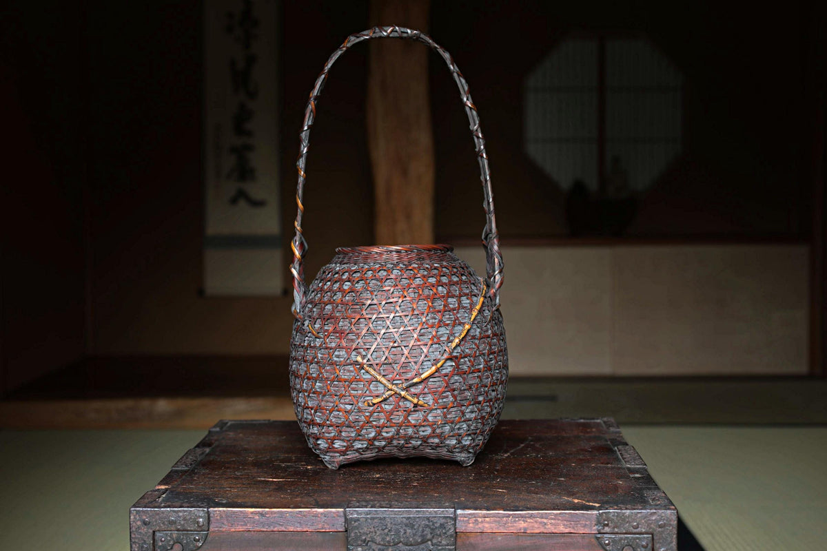 A decorative woven basket with a handle, placed on a wooden surface.