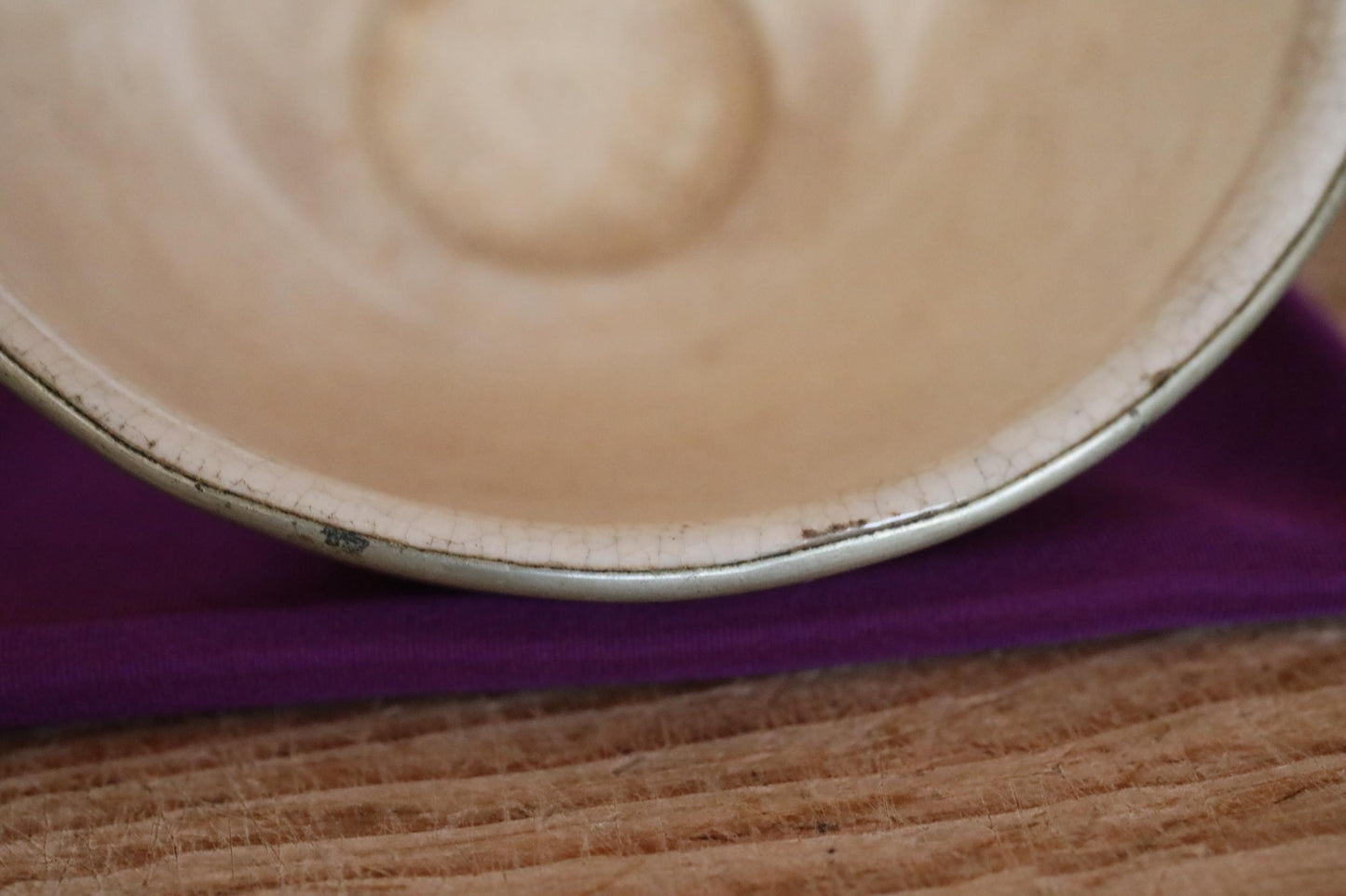 A close-up view of a white ceramic bowl with a silver rim, resting on a purple cloth on a wooden surface.