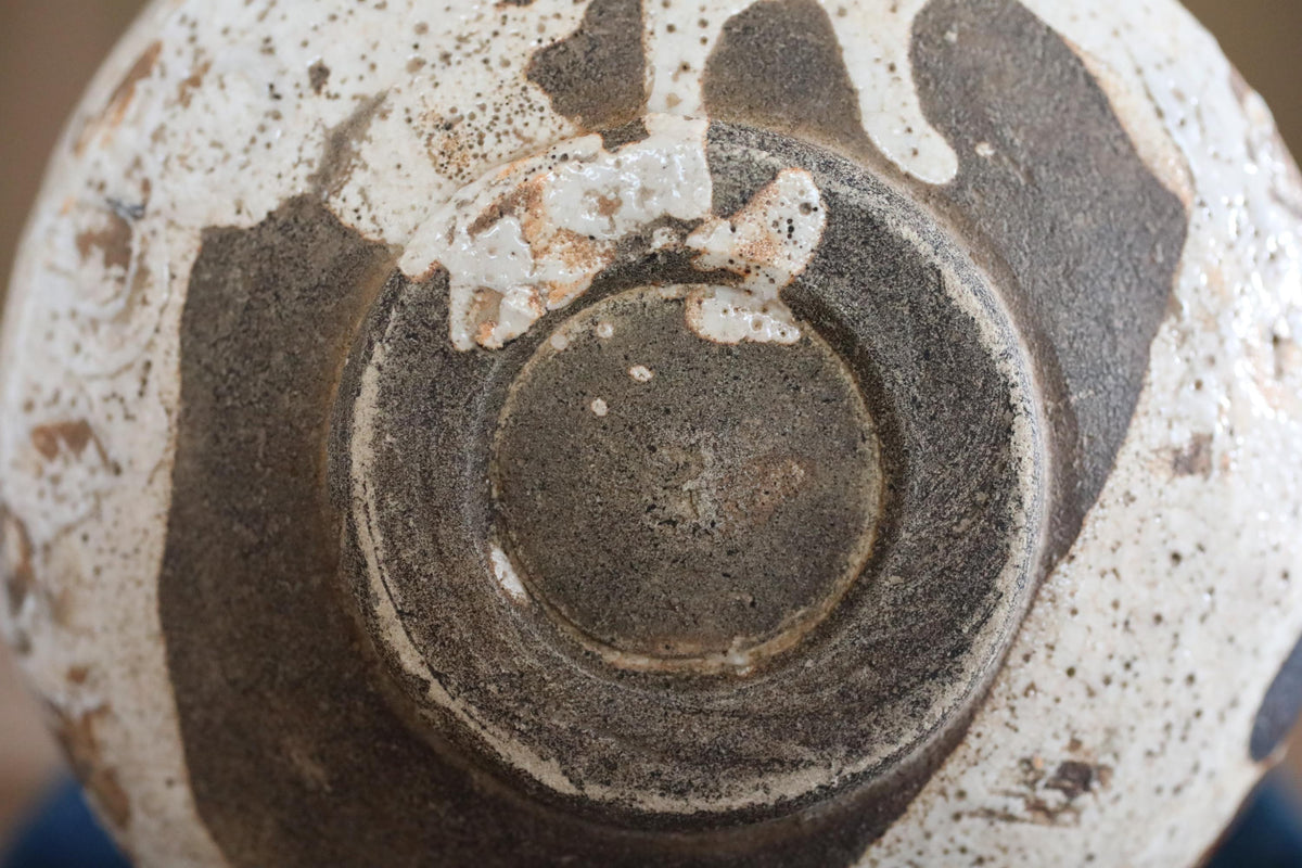 A close-up view of a ceramic or metal object with a textured surface, featuring a circular or oval shape and a dark, speckled pattern.
