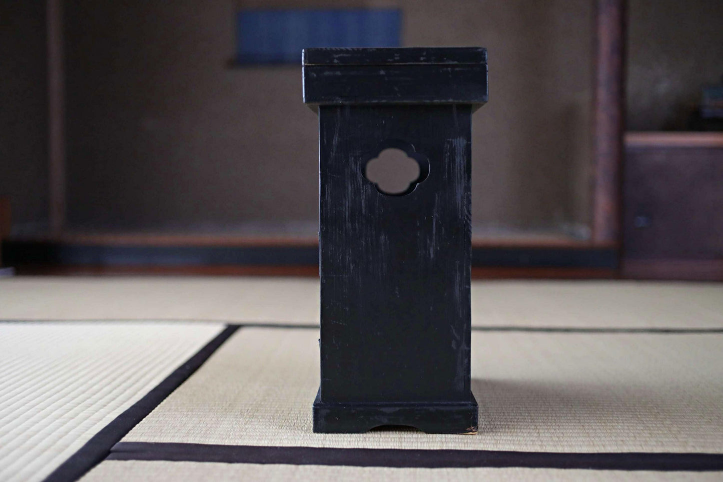 A black wooden object with a circular cutout on the top, placed on a white mat with a black border.