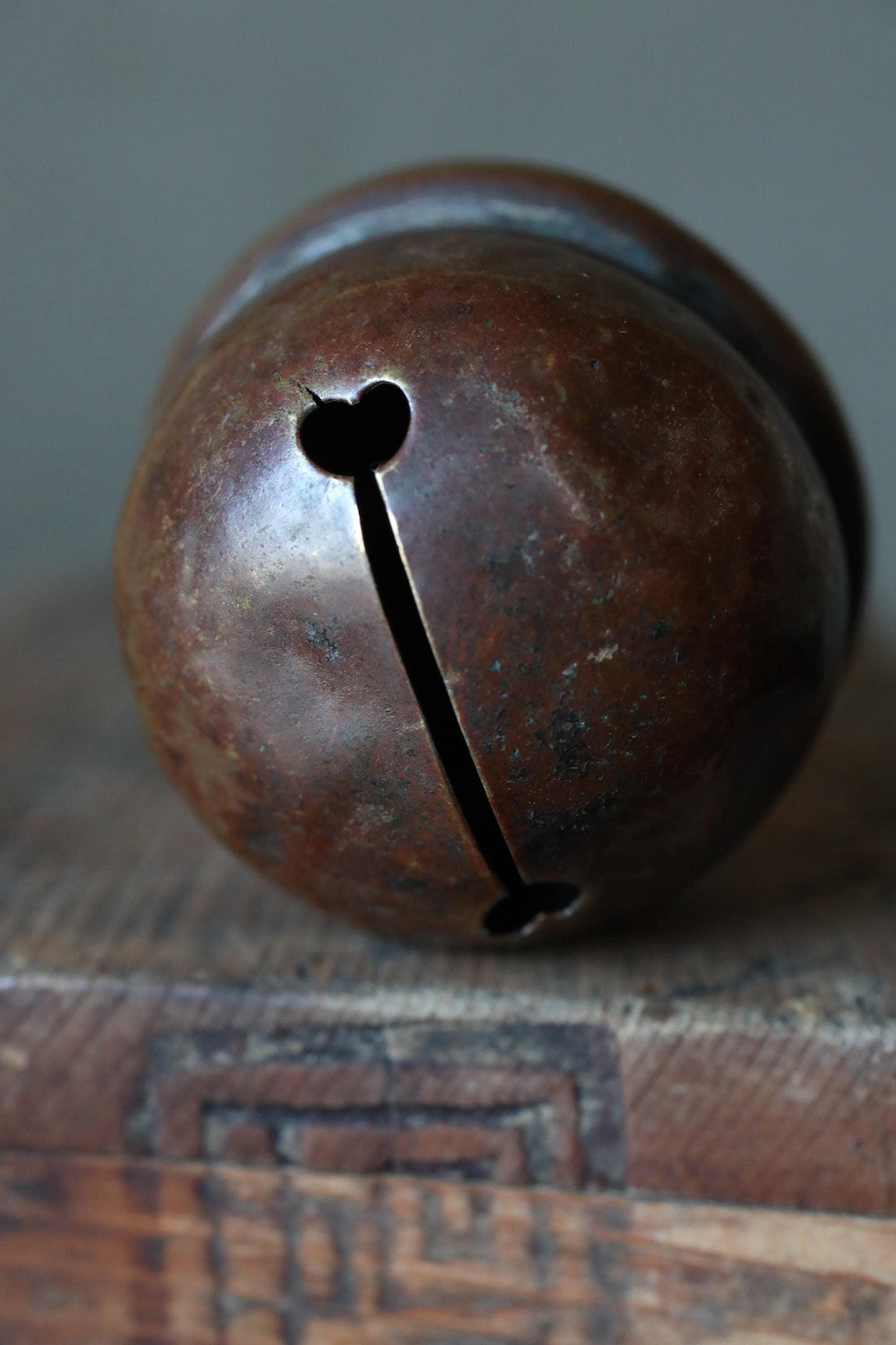 A close-up image of a rusted metal bell with a heart-shaped cutout, resting on a wooden surface.