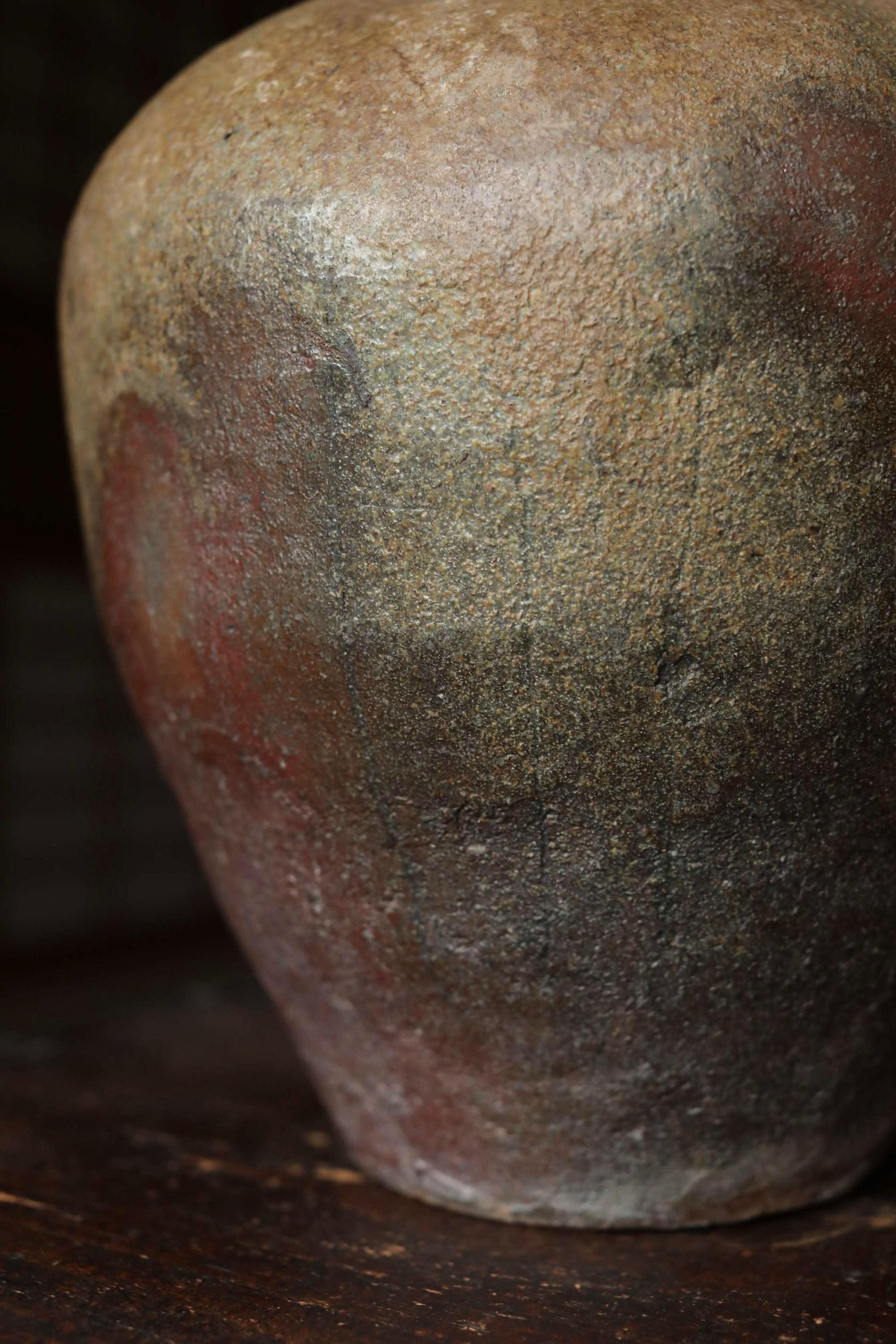 A close-up image of a weathered, textured vase or urn with a reddish-brown hue and a rough, uneven surface.