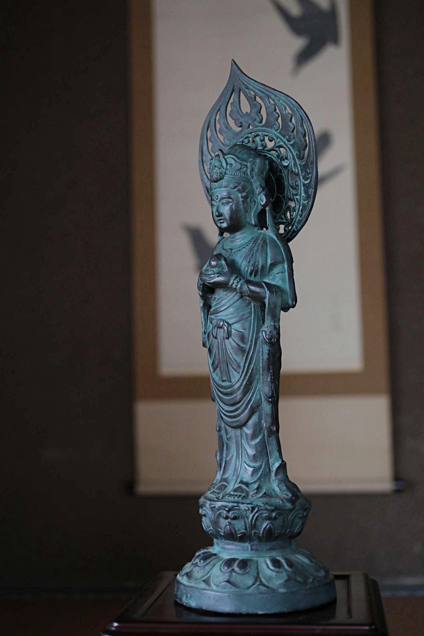A bronze statue of a Buddhist deity, likely a Buddha figure, is displayed on a wooden pedestal in the foreground of the image.
