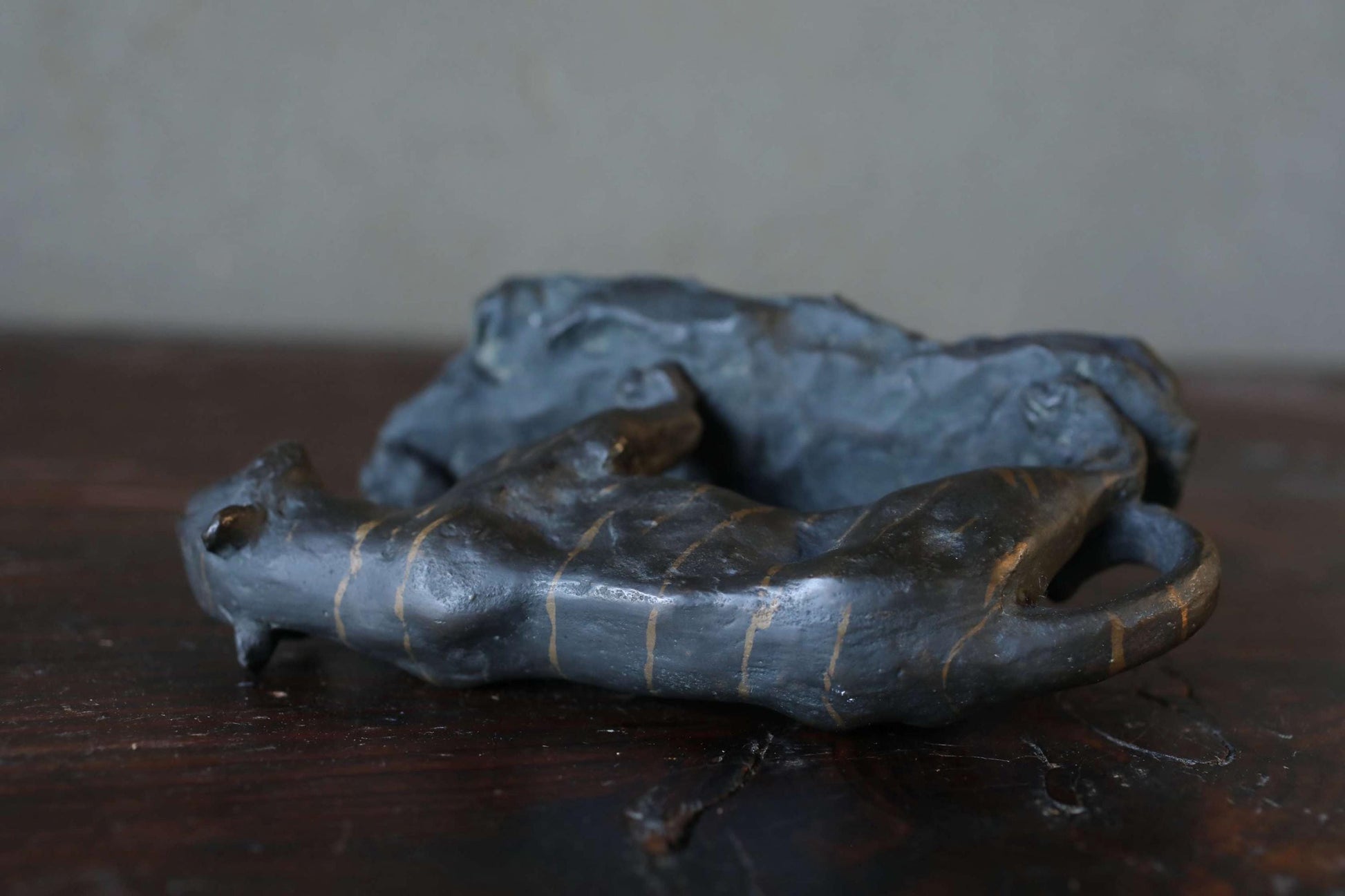 A dark-colored metal sculpture of a cat or feline figure is displayed on a wooden surface.