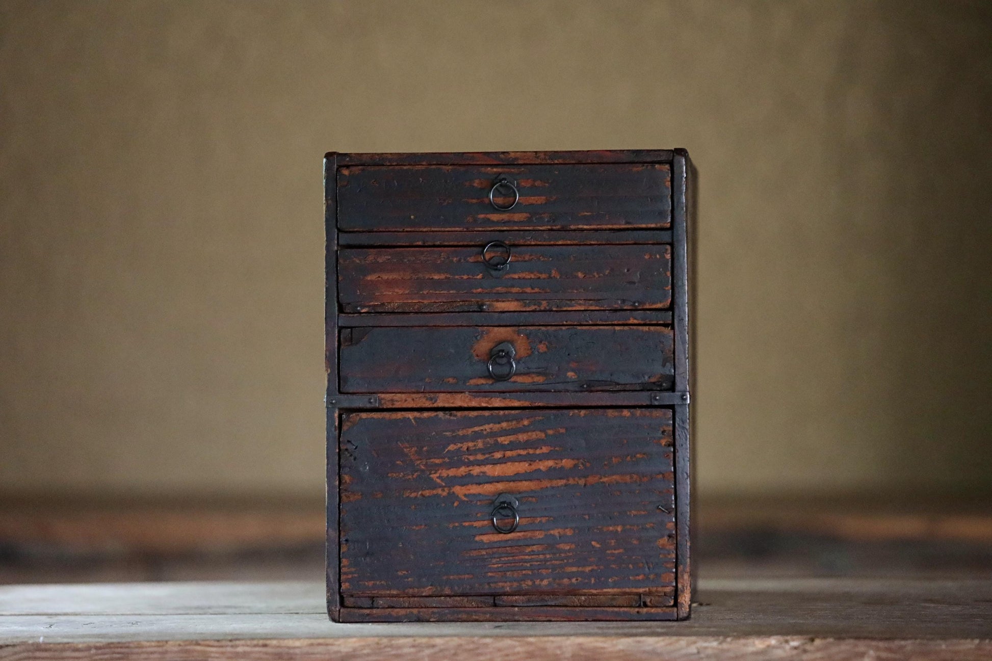An old, weathered wooden chest of drawers with four drawers, standing alone on a wooden surface against a plain background.