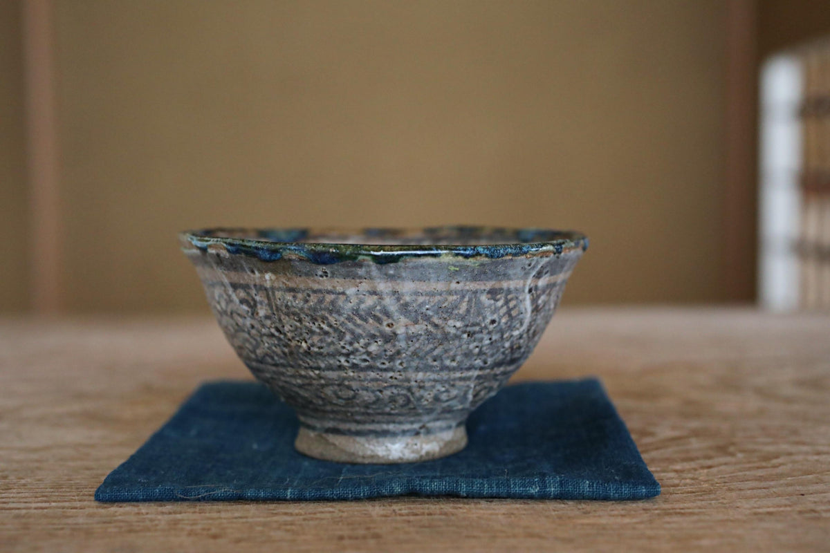 A ceramic bowl with a blue and white patterned design sits on a blue cloth on a wooden surface.