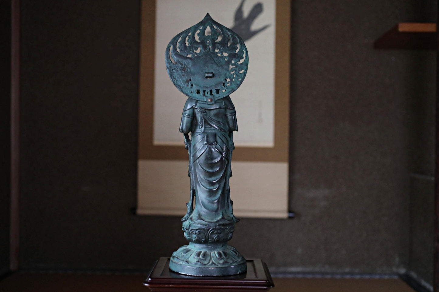 A bronze statue of a deity, possibly a Buddha, is displayed on a wooden stand in the center of the image.