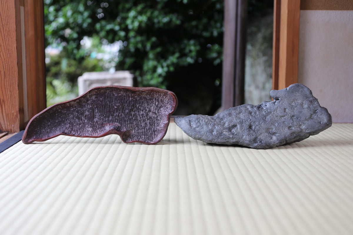 Two natural stone objects, one dark and one light, are placed on a wooden surface, with a blurred natural background.