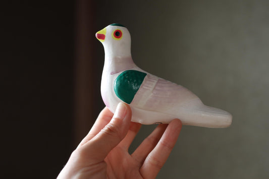 A hand is holding a colorful ceramic bird toy, which appears to be a small, white and green bird with a yellow beak.