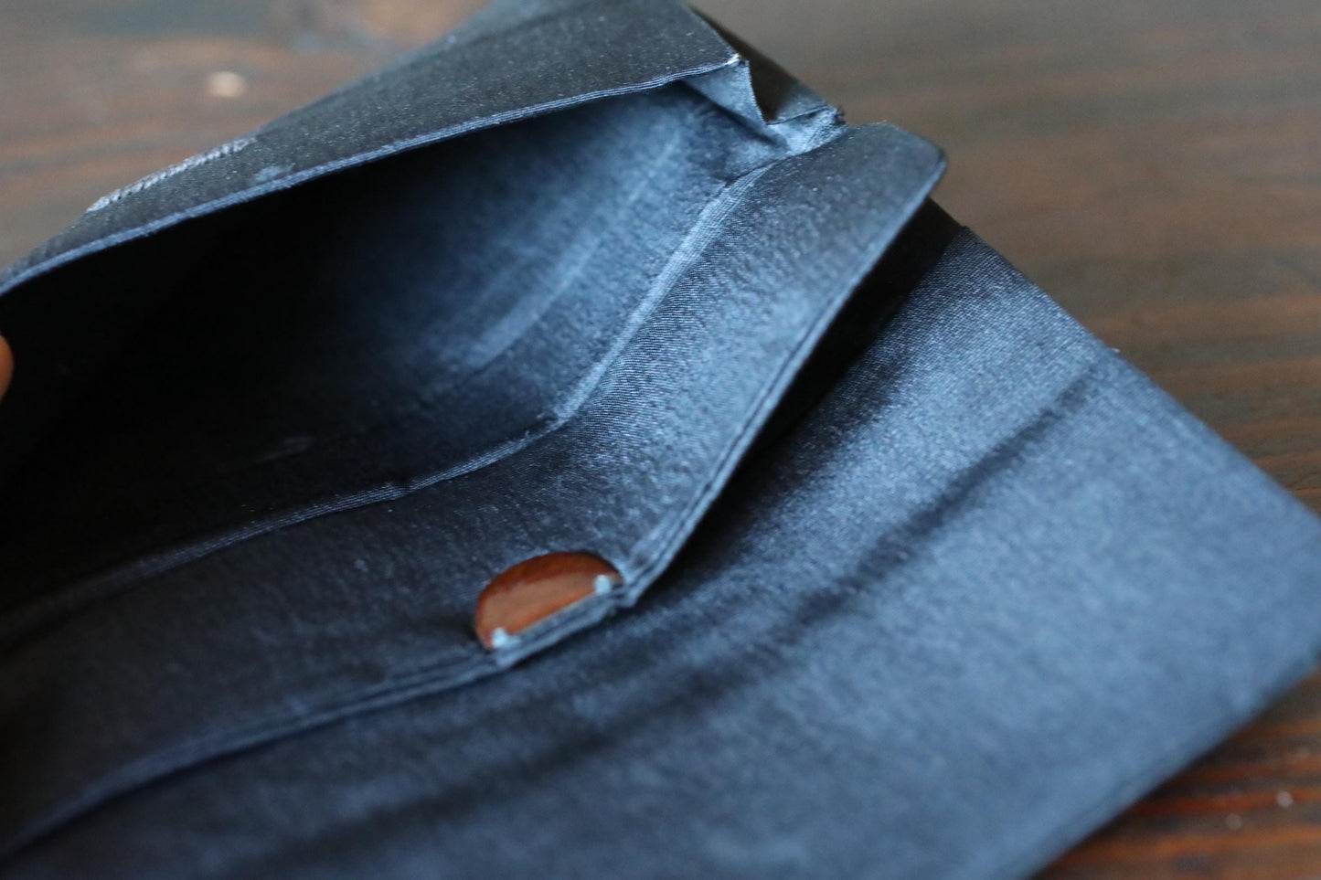 a close-up view of a black wallet or card holder with a brown button on the front.