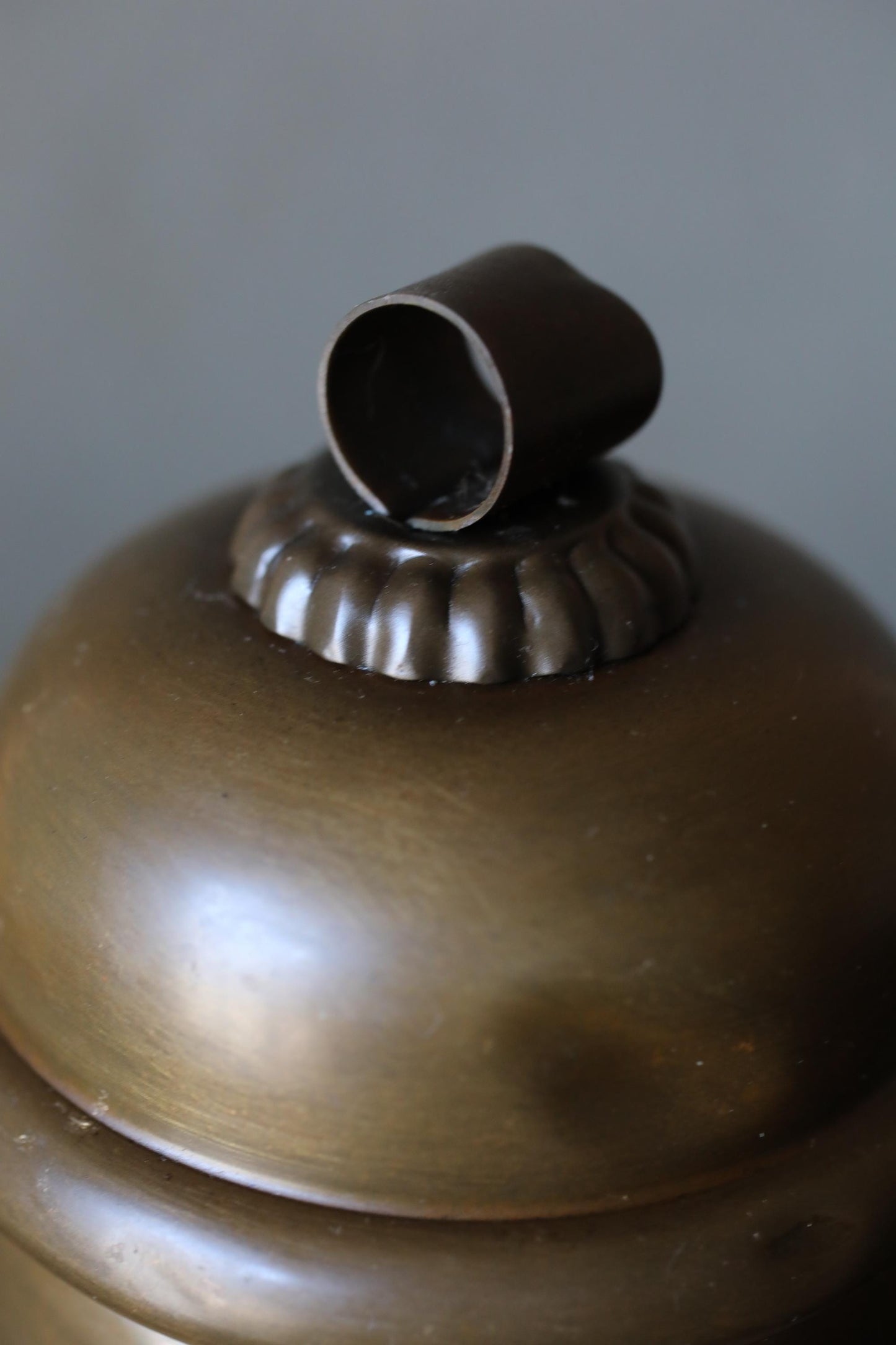 A close-up image of a brass-colored lampshade with a small metal piece on top.
