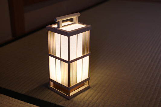 A white, rectangular lantern with a handle on top, placed on a woven mat.