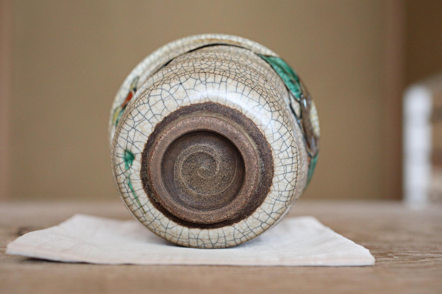 A ceramic vase with a white and brown patterned design sits on a white cloth on a wooden surface.