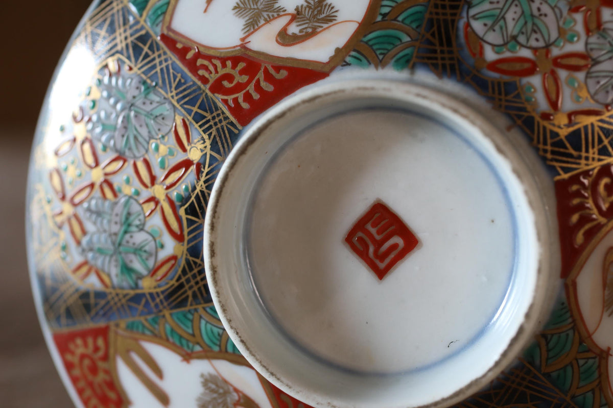 a close-up view of a decorative ceramic bowl or plate with intricate patterns and designs. The bowl has a red and white color scheme and a small red symbol or logo on the center.