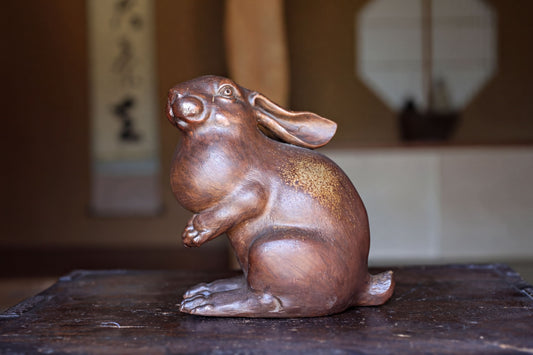 A bronze statue of a rabbit sitting on a wooden surface.