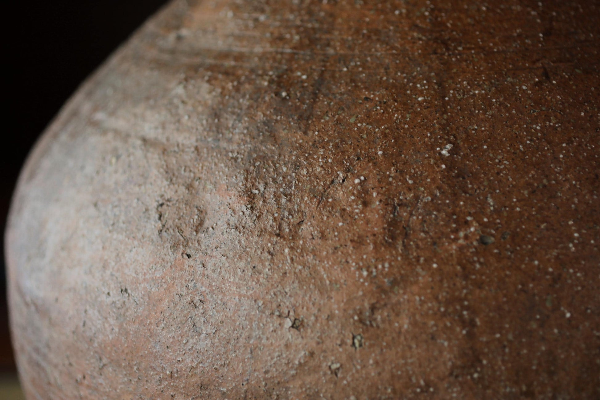 A close-up image of a large, brown, textured clay pot or vase with visible cracks and crevices.