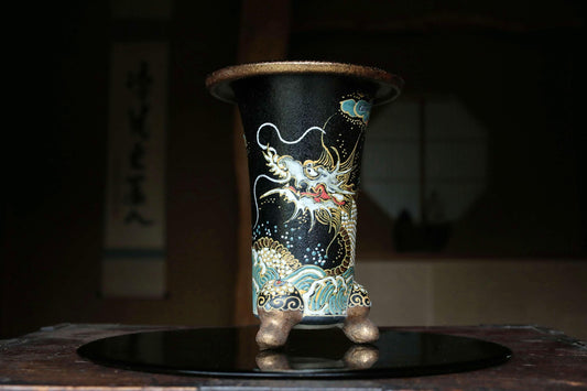 A black vase with a dragon design on it, placed on a black surface.