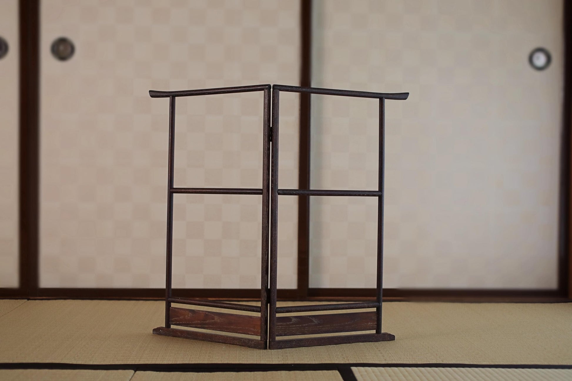 a wooden folding chair with a black metal frame, placed on a tatami mat in front of a traditional Japanese sliding door.