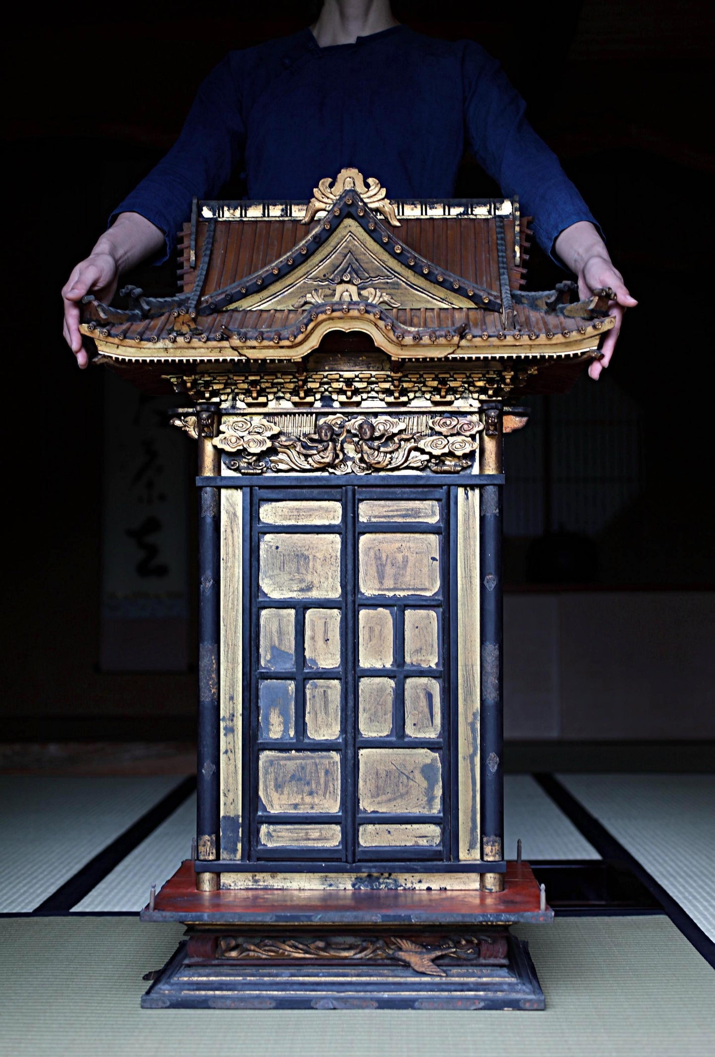 A person is standing behind a decorative wooden structure with intricate gold and black details, which appears to be a traditional Japanese temple or shrine.