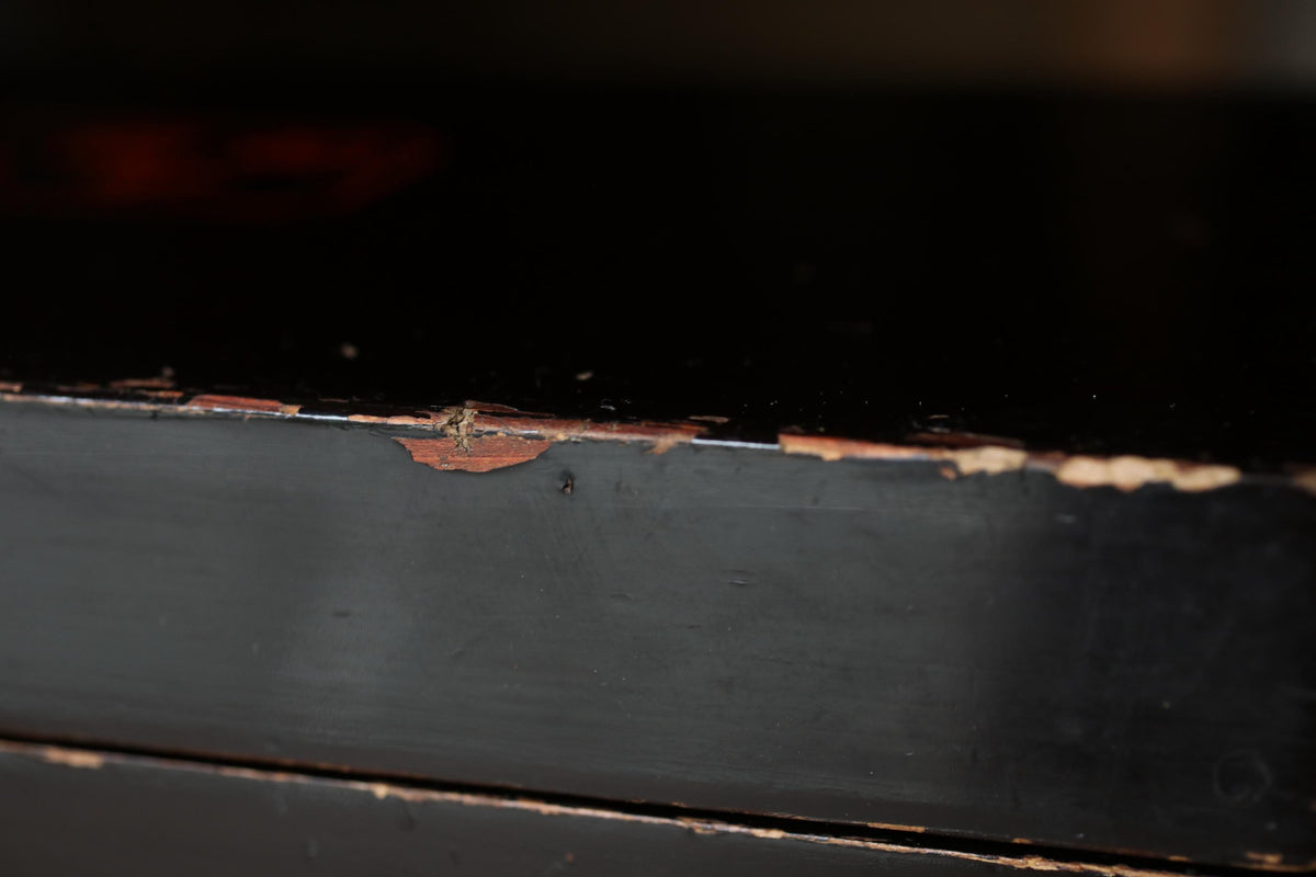 a close-up view of a black surface with a chipped and worn paint, revealing the underlying wood grain.