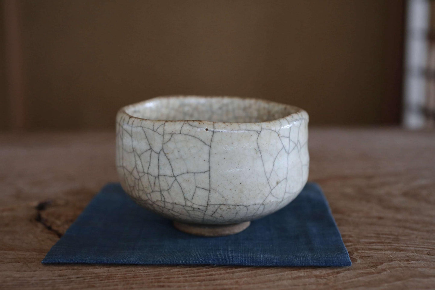A white ceramic bowl with a cracked texture sits on a blue cloth on a wooden surface.