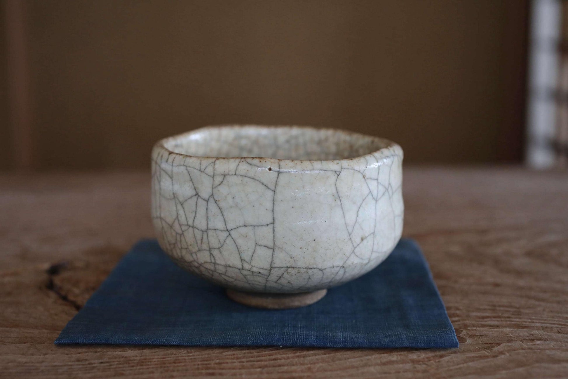 A white ceramic bowl with a cracked texture sits on a blue cloth on a wooden surface.