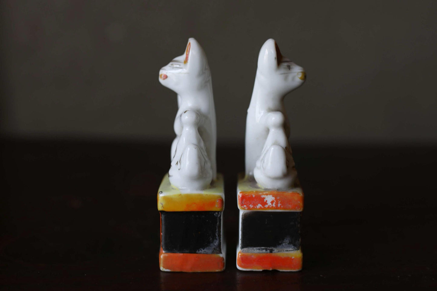 Two white ceramic cat figurines standing on colorful blocks against a dark background.