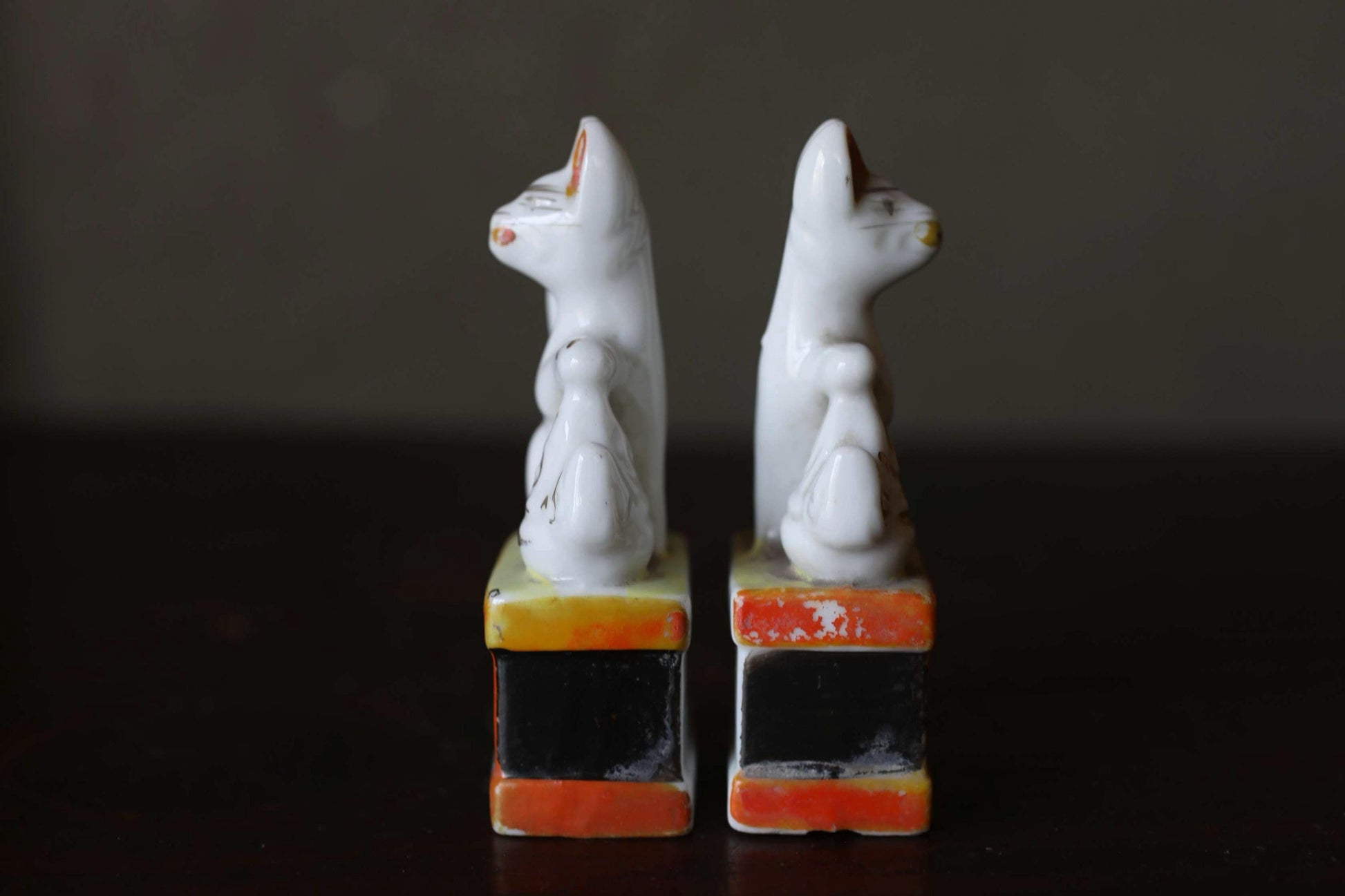 Two white ceramic cat figurines standing on colorful blocks against a dark background.