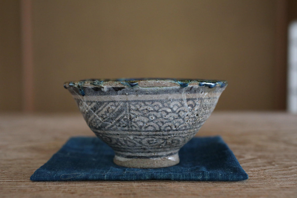 A decorative ceramic bowl with intricate patterns sits on a blue cloth on a wooden surface.