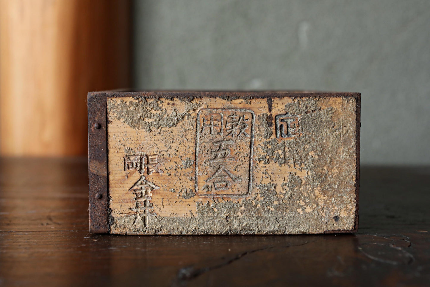 An old, weathered wooden box with Chinese characters and symbols carved into it, sitting on a wooden surface.