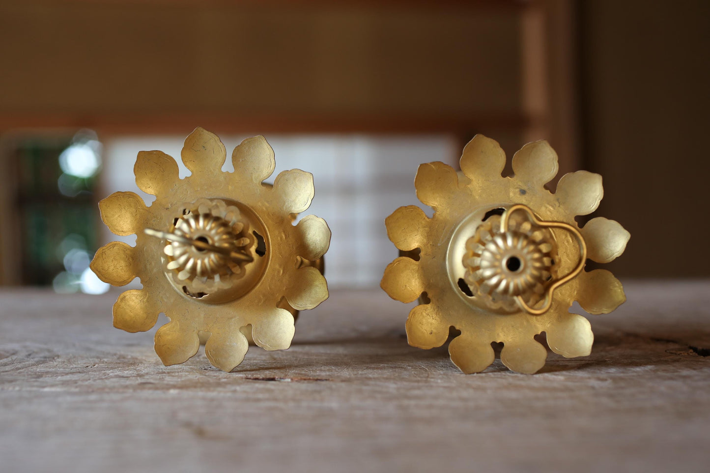 two ornate golden candle holders with intricate flower-like designs, placed on a wooden surface.