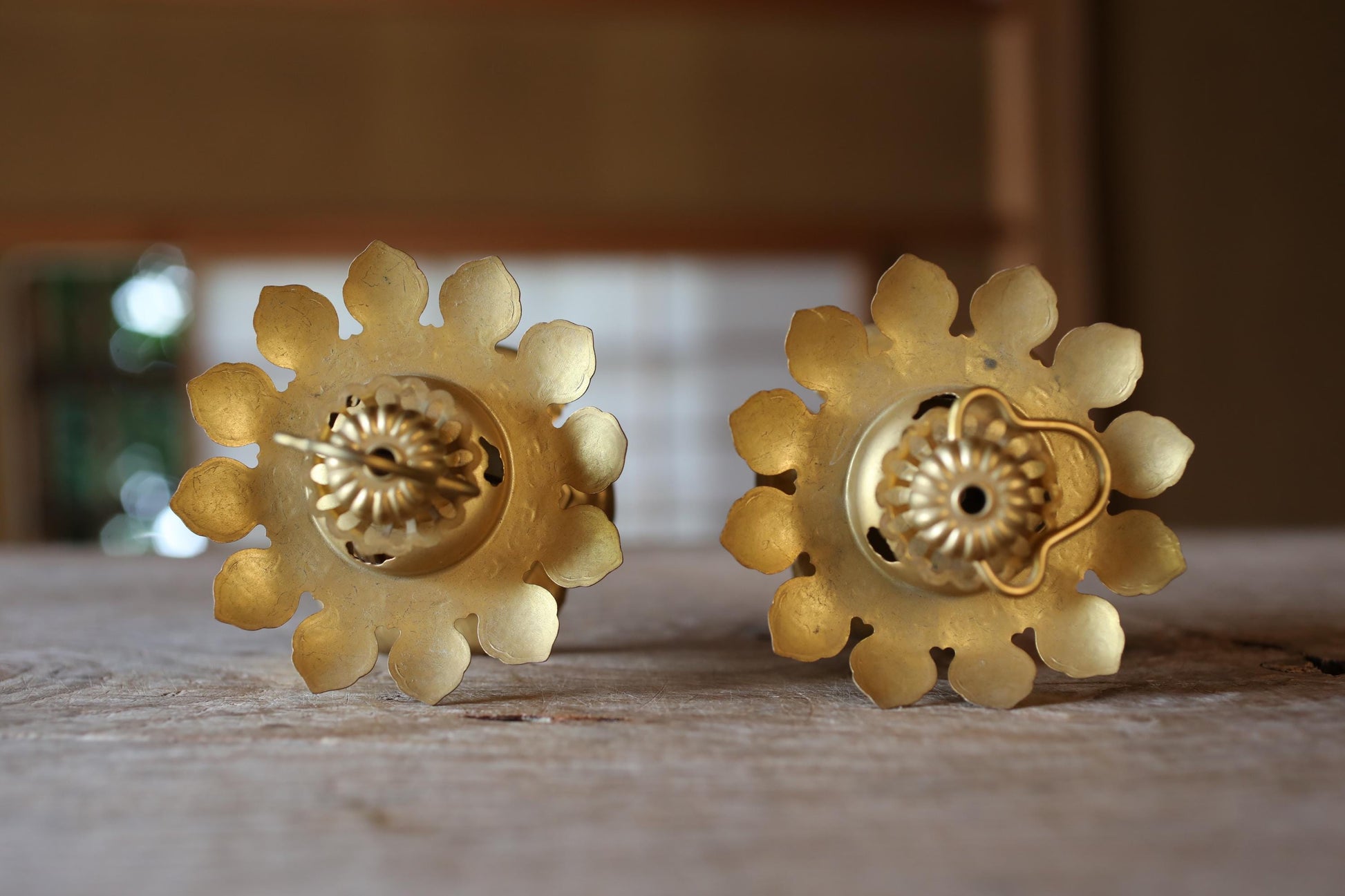 two ornate golden candle holders with intricate flower-like designs, placed on a wooden surface.