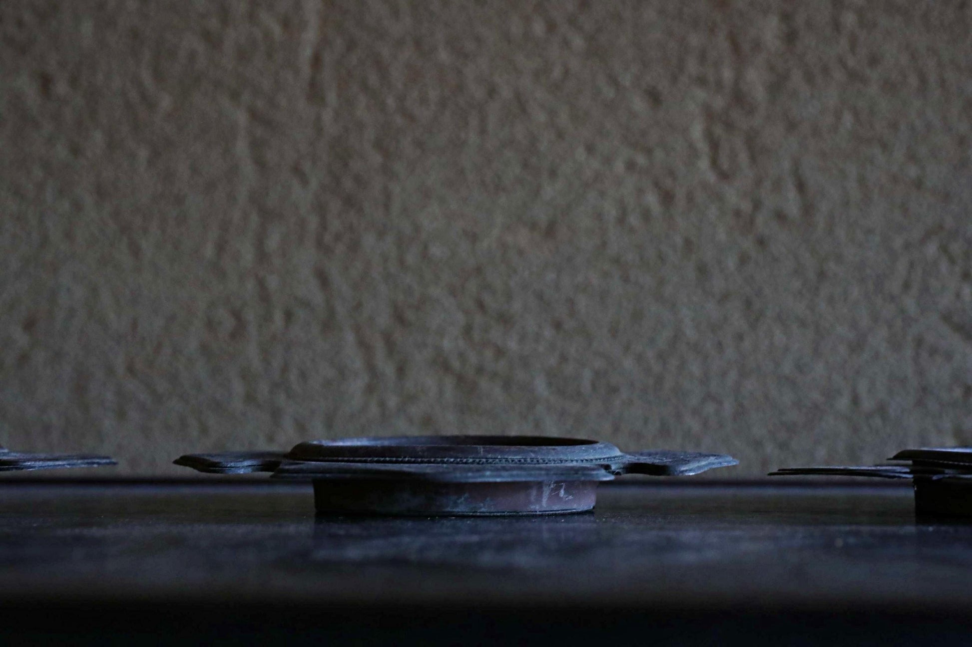 a close-up view of a dark metal object, possibly a piece of furniture or a decorative item, placed on a dark surface against a textured background.