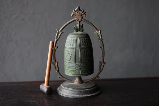 An antique green bell with a decorative metal frame and a wooden mallet is displayed on a dark surface.