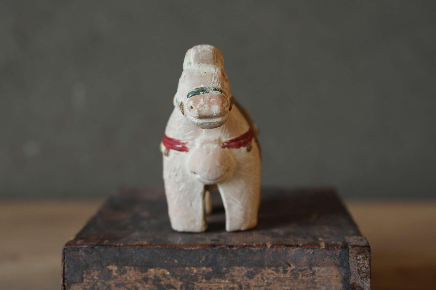 A small, white wooden toy horse with a red ribbon around its neck is sitting on a wooden surface.