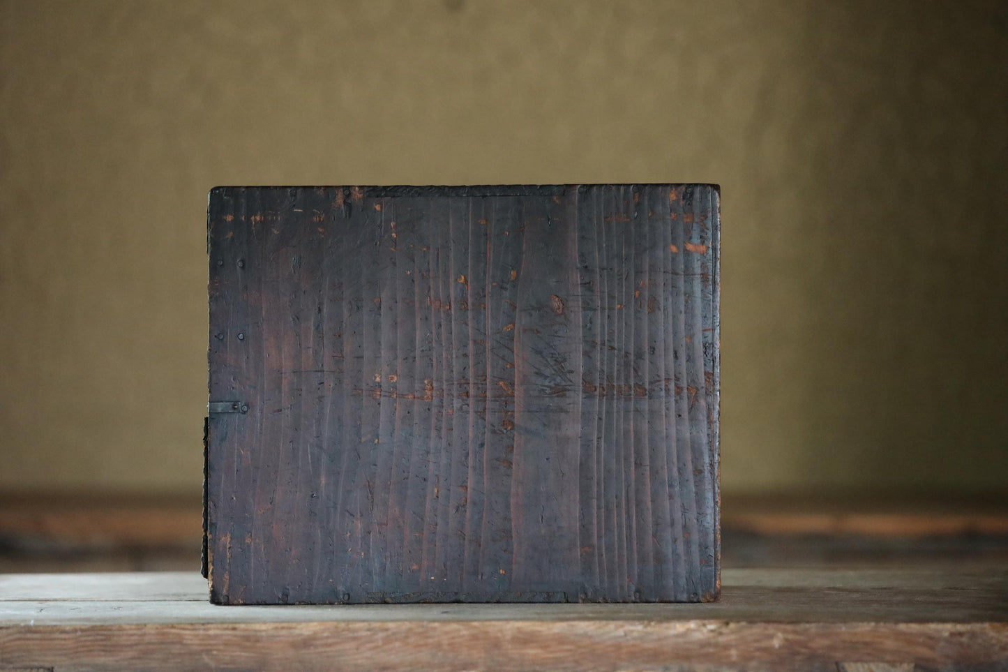 A dark wooden block or block of wood is sitting on a wooden surface.