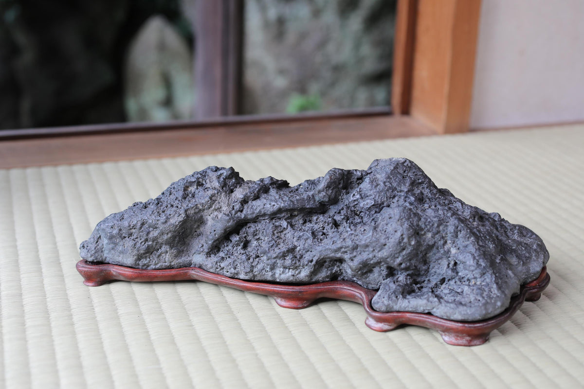 A large, gray rock sits on a wooden base, placed on a white mat.