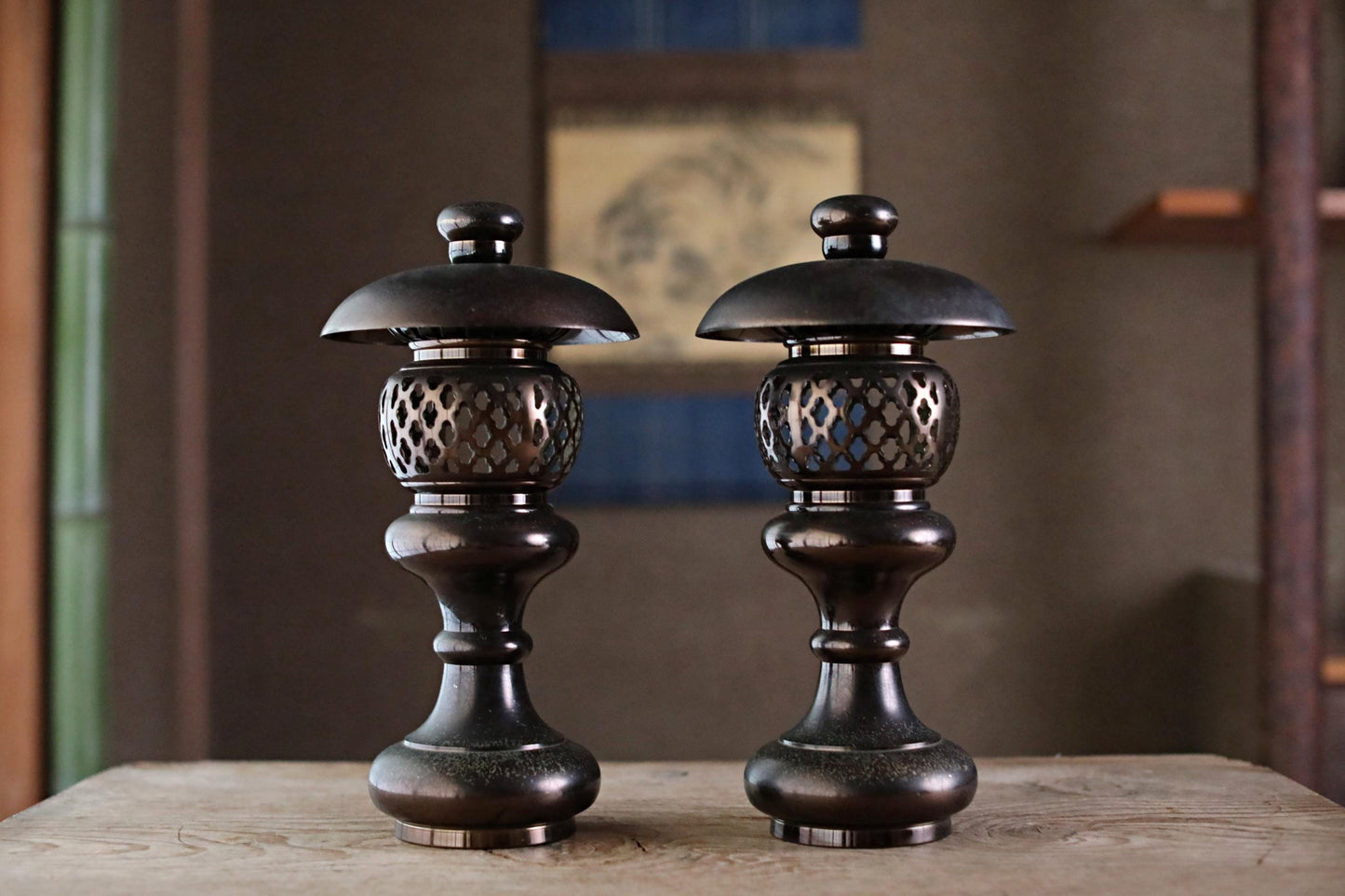 Two ornate, black metal lanterns with intricate designs stand side by side on a wooden surface.
