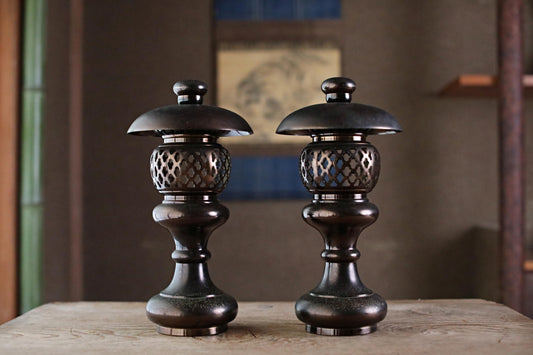 Two ornate, black metal lanterns with intricate designs stand side by side on a wooden surface.