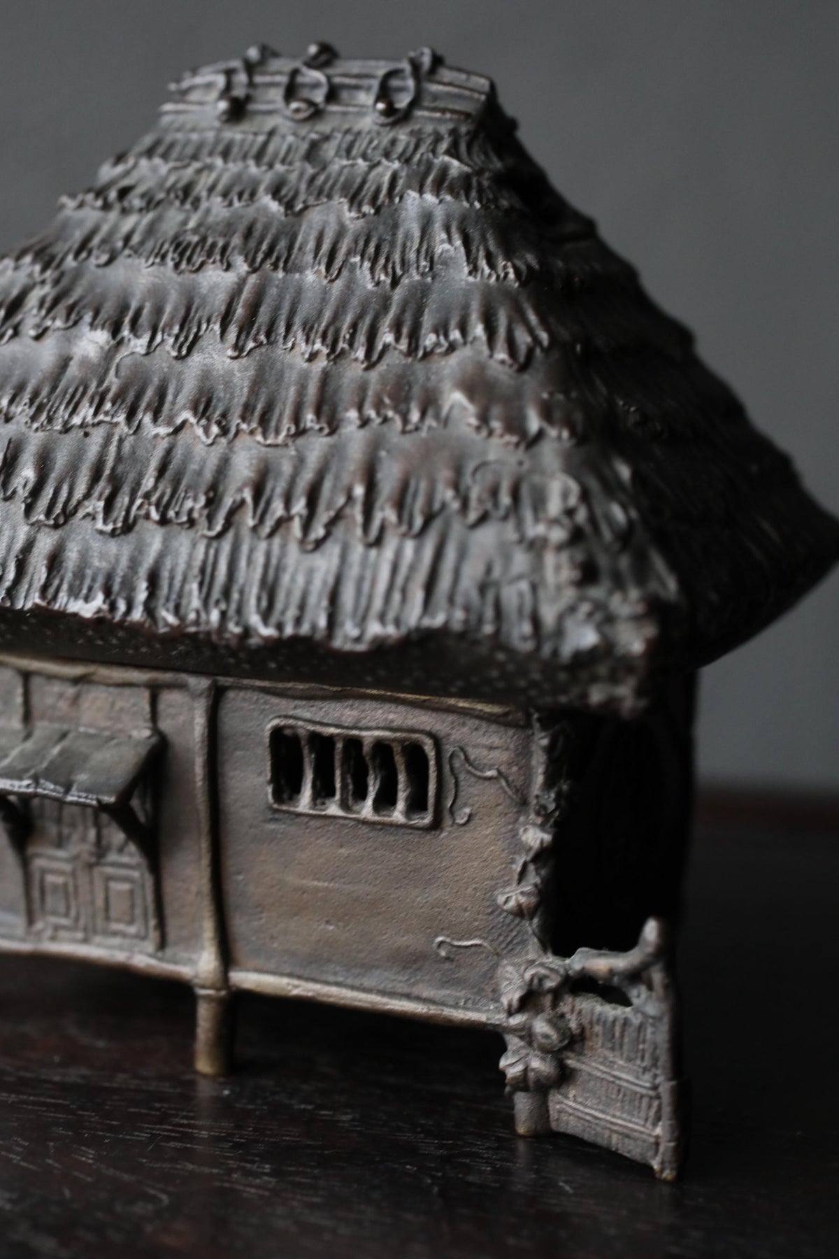 A small, intricately designed metal figurine depicting a traditional thatched roof house.