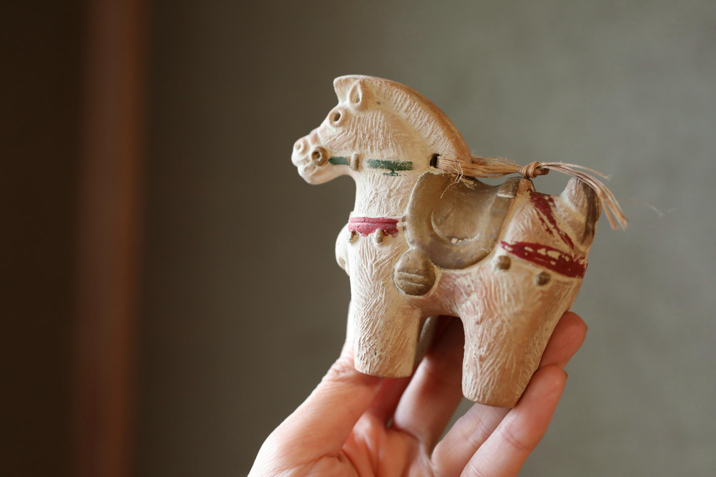 A hand holding a small, white ceramic figurine of a horse.