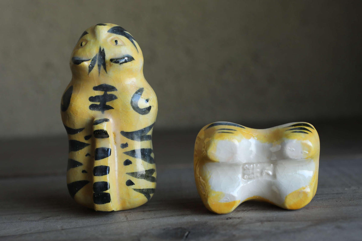 Two ceramic figurines, one with a yellow and black striped pattern and the other with a white and black striped pattern, are displayed on a wooden surface.