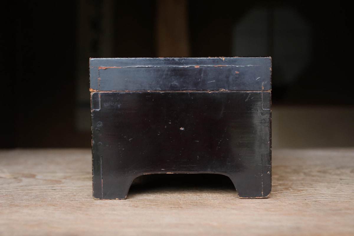 A black wooden box with a weathered, rustic appearance sits on a wooden surface.