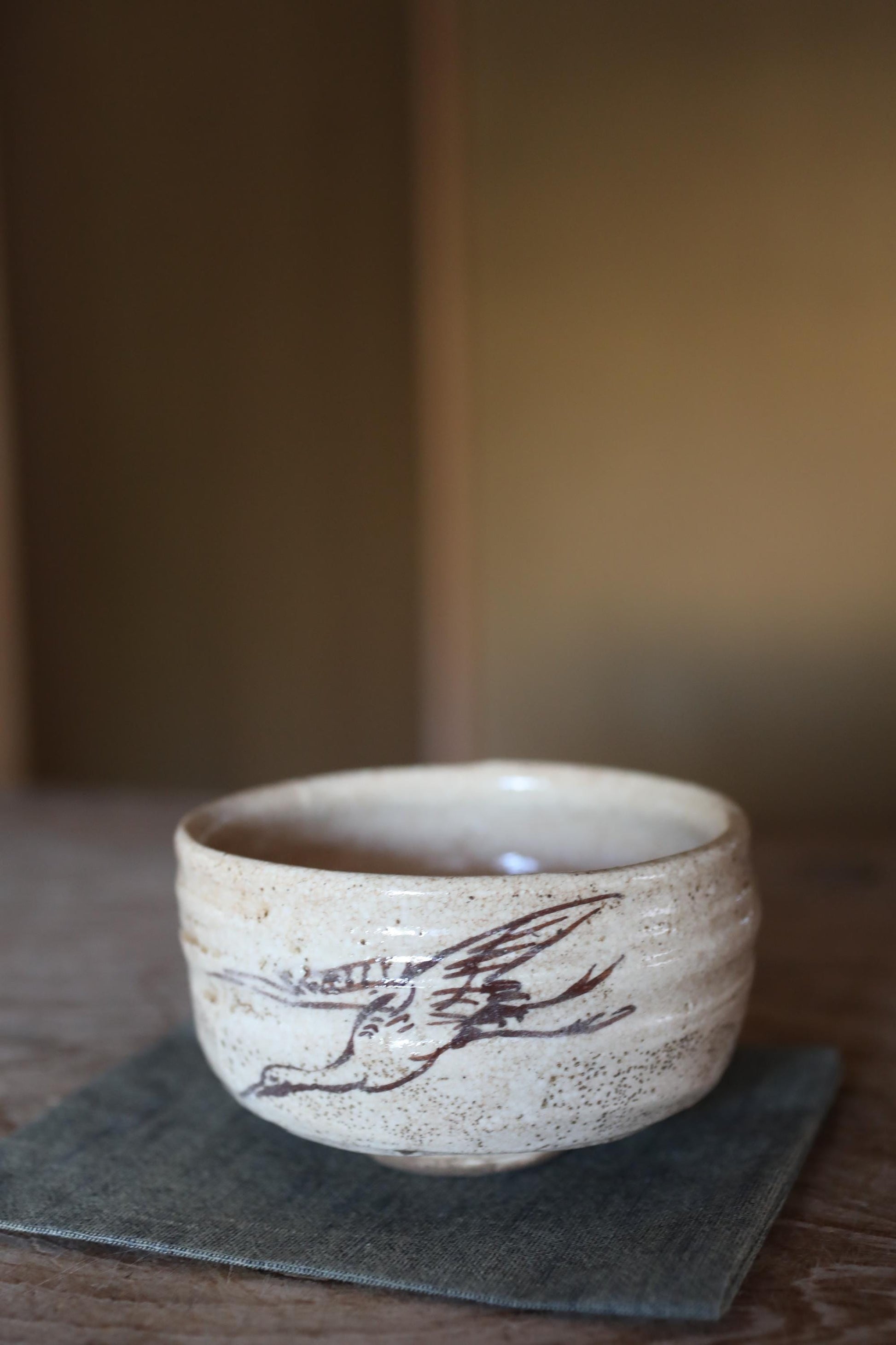 A ceramic bowl with a bird design on it, sitting on a gray cloth on a wooden surface.