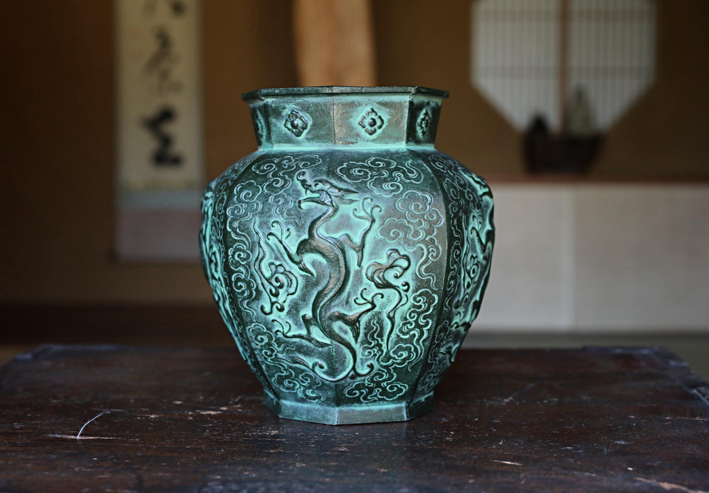 A decorative green vase with an intricate dragon design sits on a wooden surface.