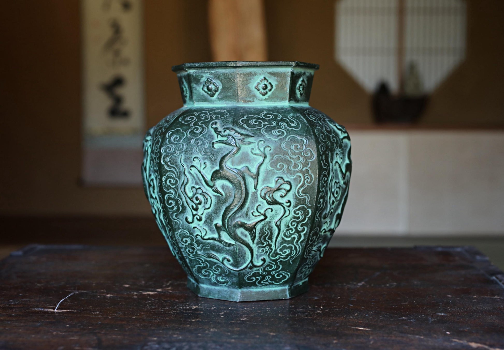 A decorative green vase with an intricate dragon design sits on a wooden surface.